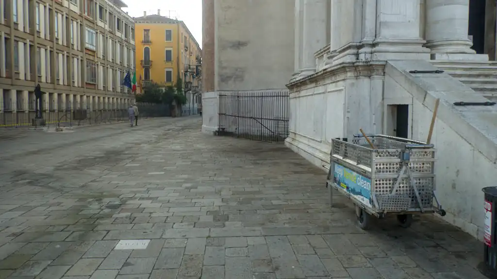 The small square besides a church, with a different stone in the pavement. To the right also a rubbish cart left by the street cleaners.